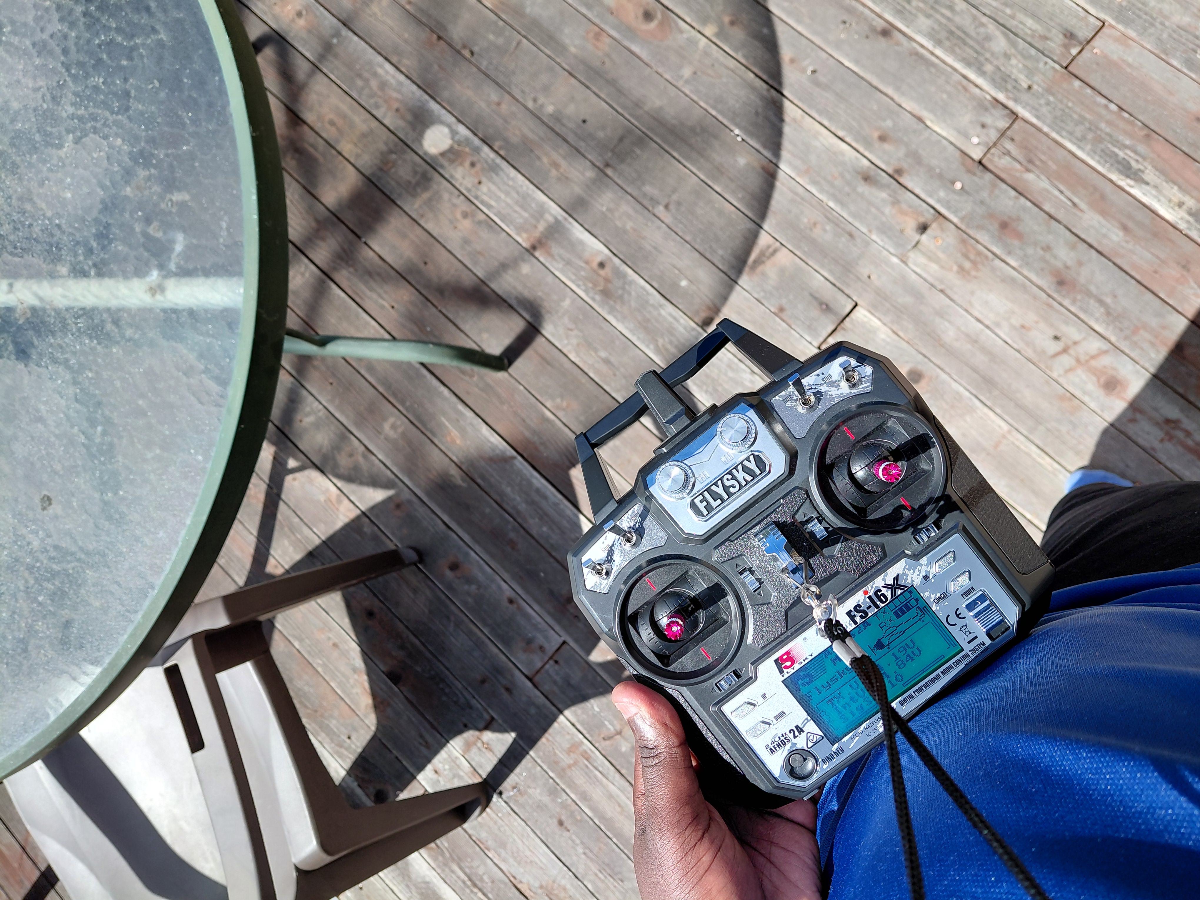 Hands holding a FlySky RC transmitter on a wooden deck outdoors
