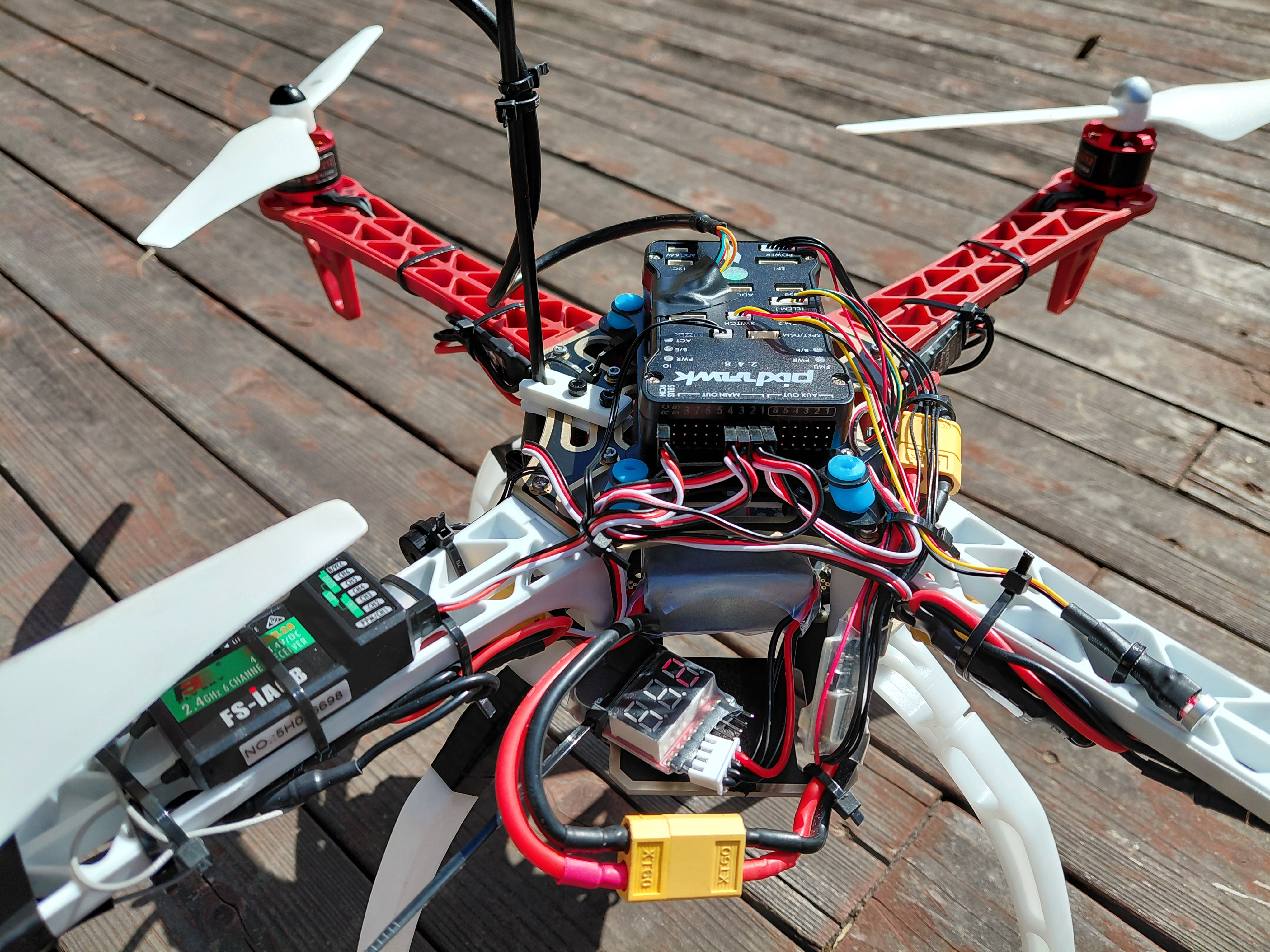 Custom quadcopter frame with Pixhawk flight controller, wiring, and propellers on a deck